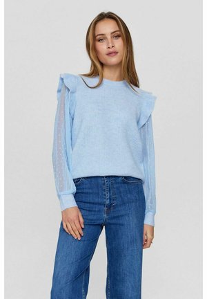 Light blue sweater with ruffled shoulders, paired with sheer, dotted blue sleeves. Worn with high-waisted blue jeans.