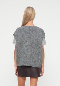 Grey knitted sweater with a loose fit, short sleeves, and a textured surface, styled over a light grey top and a dark leather skirt.