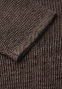 Tessuto marrone strutturato con un motivo a coste e un bordo piegato. Il materiale appare morbido con una tessitura uniforme in tutto.