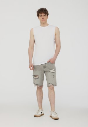 Canotta bianca abbinata a pantaloni corti in denim chiaro con effetto usurato, caratterizzati da orli frangiati e multiple strappi. Sneakers bianche casual.