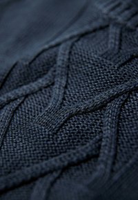 Dunkelblauer Strickpullover-Stoff mit komplexen Texturmuster und hervorgehobenen Kabeln, der ein einheitliches Gewebe und ein weiches Aussehen präsentiert.
