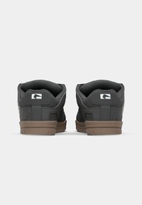 Black sneakers featuring a textured upper, rounded shape, and brown rubber soles. A logo is visible on the heel, with subtle accents.