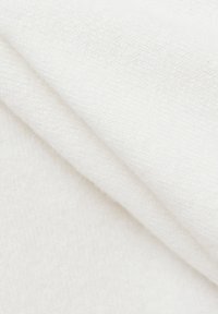 Prim-plan al unui material moale, alb, cu țesătură fină și ușoare cute, evidențiind textura și aranjamentul în straturi.
