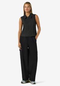 Jeans-lös ärm top med krage, framdragkedja och kontrasterande orange sömmar, ihop med lösa svarta cargobyxor och grå sneakers.