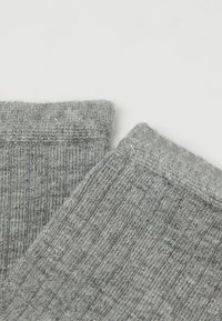 Šedé pletené ponožky s ribbovanou texturou a hladkými manžetami. Tkanina vypadá jemně s mírným leskem a ukazuje konzistentní šedou barvu po celém povrchu.