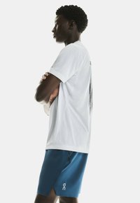 White short-sleeve t-shirt with a graphic on the back, paired with blue athletic shorts featuring a logo on the left thigh.