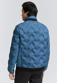 Blauer Puffer-Jacke mit einem gesteppten Muster, seitlichen Einsätzen und einem schwarzen gerippten Kragen. Das Material scheint glatt und hat eine weiche Textur.