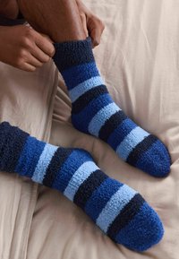 Marmuriniai pūkuoti kojinės mėlynos ir tamsiai mėlynos spalvų atspalvių, su tekstūruotu audiniu, kuriame yra skirtingo pločio horizontalių juostelių ir apvalios kojų dizainas.