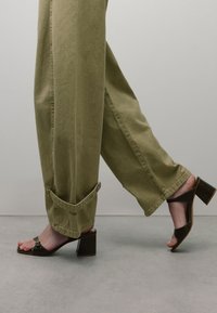 Khaki wijde broek met een omslagzoom, gecombineerd met donkerbruine open teen hakken met een vierkante hak en metalen accenten.