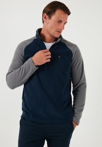 Navy blue fleece pullover with gray raglan sleeves, half-zip collar, and a small logo on the chest. Soft texture and casual fit.