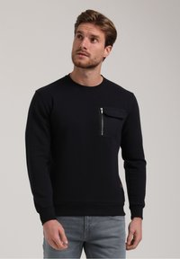 Laivastonsininen collegepaita, joka on valmistettu puuvillasta, ja siinä on vetoketjullinen rintatasku, ribbed hihansuut ja helma. Suuri pinta ja klassinen pyöreä kaula-aukko.