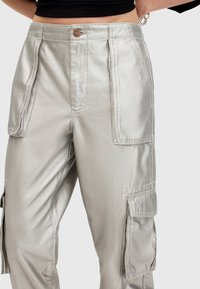 Metaliczne srebrne spodnie cargo o gładkiej fakturze, z bocznymi kieszeniami, zamknięciem na guzik z przodu oraz plisowanymi detalami.