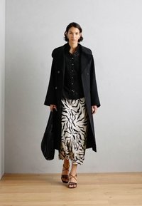 Melna dubultā krūšu mētelis, melns rakstains blūze, krēms svārki ar melniem zebra svītrām, melnas siksnu sandales un melna soma.