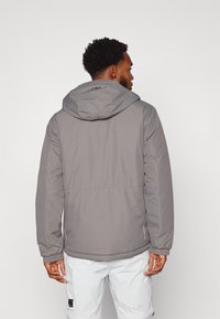 Graue Kapuzenjacke mit glatter Textur, elastischen Bündchen und geradem Schnitt. Verfügt über ein Logo am Halsausschnitt und Seitentaschen.