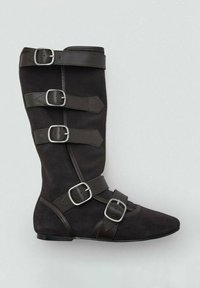 Bota de ante negra con cuatro cintas de cuero horizontales y hebillas plateadas; punta puntiaguda y suela plana; textura suave con un diseño estructurado.