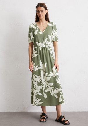 Green floral dress with white leaf patterns, short sleeves, V-neckline, cinched waist, and ankle-length hem. Paired with black sandals.