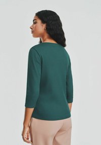 Zielona, prążkowana bluzka z długim rękawem i okrągłym dekoltem. Materiał wydaje się gładki, z dopasowanym krojem oraz rękawami o długości trzy czwarte.