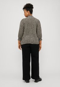 Blouse imprimé léopard noir et beige avec des manches bouffantes, tissu texturé et une silhouette légèrement ajustée, associée à un pantalon large noir.