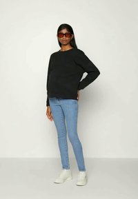 Sweatshirt preto, jeans azuis e ténis brancos. O sweatshirt tem um corte descontraído, enquanto os jeans são justos com um corte clássico.