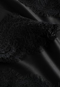 Tissu satiné noir avec une bordure en dentelle complexe aux bords ondulés et motifs délicats ; texture lisse avec des détails contrastants.