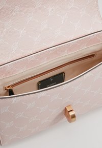 Borsa a mano rosa chiaro con superficie texturizzata, motivo floreale bianco, tasca interna e chiusura in oro. Etichetta del marchio visibile all'interno.