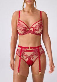 Czerwony zestaw biustonosza i pasa do pończoch z przezroczystej beżowej siateczki, ozdobiony haftem kwiatowym, złotymi akcentami, regulowanymi ramiączkami oraz detalem w postaci kokardki.