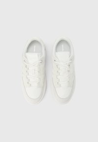 Par de zapatillas blancas de corte bajo con diseño de cordones, plantillas con marca y parte superior de textura suave, mostradas lado a lado sobre un fondo blanco.