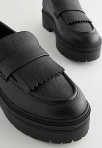  Sorte læder loafers med en tekstureret finish, der har en frynset accent og en kraftig platformsål. Glat rund tå og kontrastdetalje på sålen.