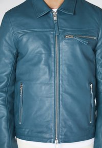 Giacca di pelle blu con colletto, dotata di zip frontale, tasche laterali e tasca sul petto con zip. Texture liscia, design aderente.
