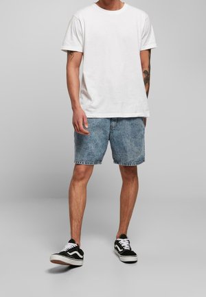 Un t-shirt en coton blanc associé à un short en denim bleu clair. Les chaussures sont des sneakers noires et blanches au design bas.