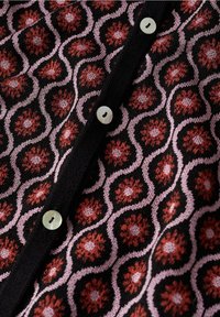 Cárdigan de punto con un patrón floral en rojo, rosa y negro, con cinco botones blancos en el frente y un acabado texturizado.