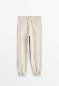 Vaaleanbeige tapered-housut, joissa on joustava vyötärö ja lahkeensuukappaleet. Ominaisuuksiin kuuluu kaksi takataskua, joissa on sileä pinta. Yksinkertainen muotoilu.