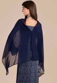 Una chalina de gasa navy se despliega sobre un vestido azul con estampado floral, que cuenta con un escote abierto. Textura suave con un diseño ligero y fluido.