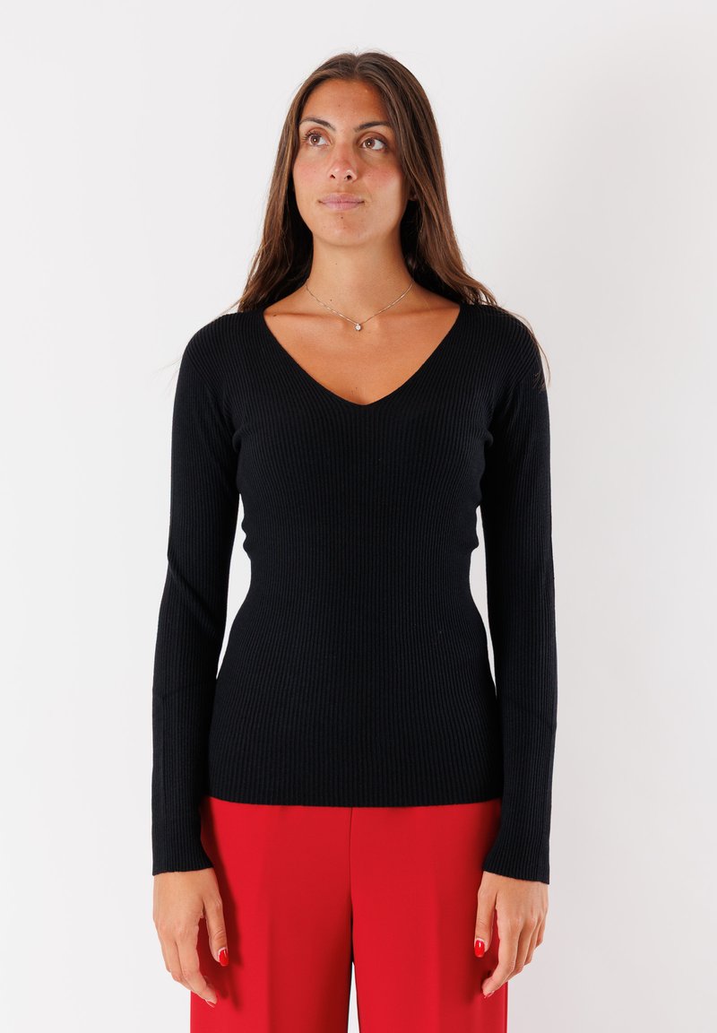 Top lungo a maniche nere a costine con scollatura a V, silhouette aderente e tessuto strutturato, abbinato a pantaloni rossi a gamba larga.