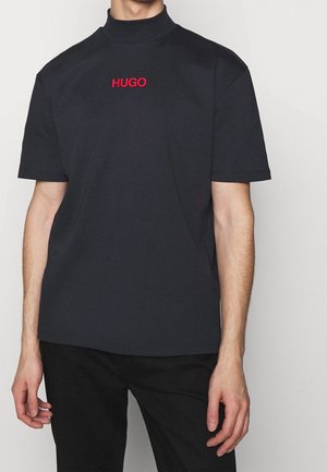 Korte ærmer navy T-shirt med høj krave, prydet med rød "HUGO" broderi på brystet. Lavet af blødt bomuldsstof.