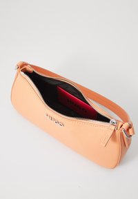 Borsa in pelle color pesca con superficie texture e zip argentata. All'interno si vede un portafoglio rosso con il marchio "HUGO". Forma compatta e cilindrica.