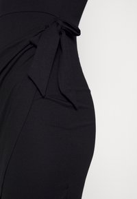 Vestido midi preto feito de tecido elástico, com um detalhe de cintura atada e textura suave, apresentando um silhueta justa.