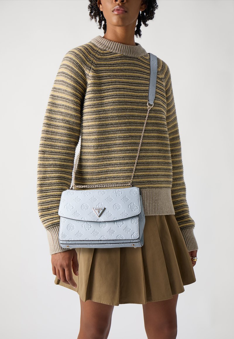Light blue textured handbag with a flap cover and silver logo detail. The strap is chain-linked, complementing a striped sweater and khaki skirt.