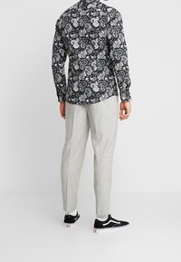 Maglietta nera a maniche lunghe con stampa paisley bianca, abbinata a pantaloni tapered grigi chiari e sneakers nere con dettagli bianchi.