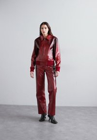 Röd läderjacka med dragkedja och krage, kombinerad med matchande högmidjade byxor. Texturerad yta och figurnära design, kompletterad med svarta stövlar.