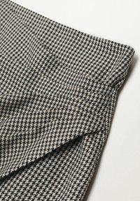 Tela con patrón de pata de gallo en blanco y negro, con una textura suave y borde doblado, que muestra detalles de diseño geométrico distintivos.