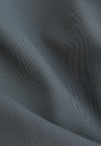 Gros plan d'un tissu gris avec une fine texture côtelée et des plis doux créant des ombres et des reflets délicats.