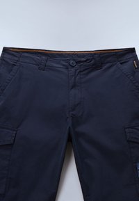 Tummansiniset cargo-housut, jotka on valmistettu puuvillasekoitekankaasta, ja joissa on nappisuljenta, useita taskuja sekä oranssi koriste vyötäröllä.