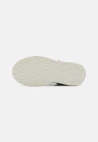 Semelle de chaussure de couleur claire avec des motifs d'étoiles et d'éclats de soleil, dotée de grips texturés et de détails de marque. Matériau lisse et durable.