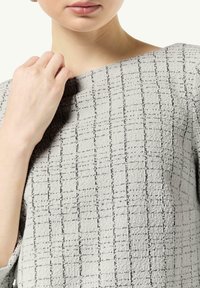 Jasnoszara bluzka z teksturowanym wzorem czarnych kwadratów. Projekt posiada dekolt typu off-shoulder oraz miękką, tkaną strukturę.