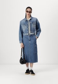 Jeansjacka med långa ärmar, blå cargokjol och randig skjorta. Accessoarer med svart handväska och sneakers med vita accenter.