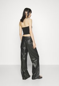 Zwart crop top met een aansluitend ontwerp en een blootgestelde rug, gecombineerd met luchtige, zwarte leren broek met hoge taille en zichtbare zakken.