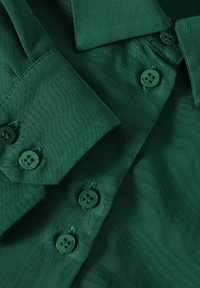 Green collared shirt textured fabric with button closure, featuring matching green buttons and visible stitching details.