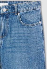 Jasnoniebieskie dżinsy z wyblakłą teksturą, z przednią kieszenią, metalowym guzikiem i pomarańczowymi przeszyciami wzdłuż szwów.