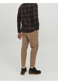 Camicia a maniche lunghe a scacchi marrone e nera, abbinata a pantaloni in velluto a coste color beige e stivaletti alla caviglia in suede nero. Presenta cuciture visibili e tasche.